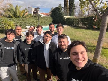 A group of smiling young people pose for a photo outdoors on a grassy lawn, several wearing black 'xneeti' hoodies.