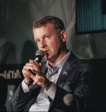 The image features a man sitting down wearing a suit jacket and holding a microphone. The background of the photo shows a blue wall with a window behind him. There are also two microphones visible, one being held by the man and another placed on the table in front of him. The text "At @proofoftalk this week in Paris" is present in the image, indicating that the event taking place might be related to data privacy or security.

The post seems to discuss the importance of reliable, compliant, and scalable infrastructure for institutions. It highlights the need for organizations to adapt their systems to future advancements in technology while ensuring data privacy and security. The man holding a microphone could be an expert on this topic, possibly speaking at the event or sharing his insights with others through the post.