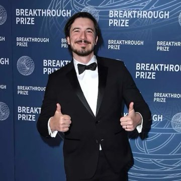 A man in a black tuxedo giving two thumbs up on the red carpet at the Breakthrough Prize event.