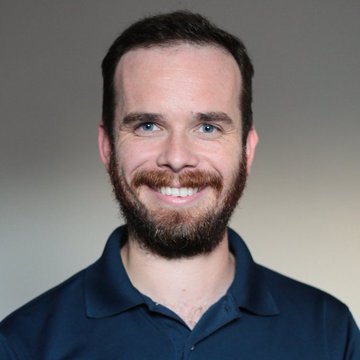A professional headshot of a smiling man with a brown beard wearing a dark blue polo shirt.