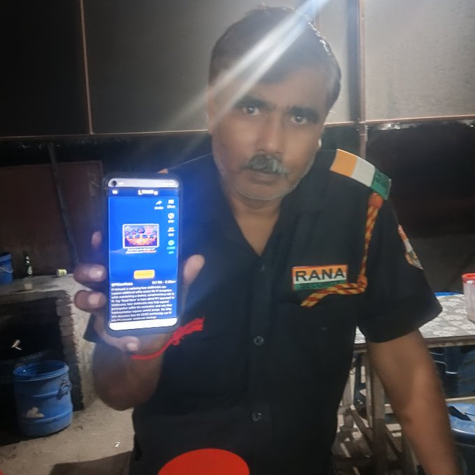 A man in a black 'RANA POLICE' uniform displays a smartphone showing a game or app interface with the numbers '01 02 10 01 15.'