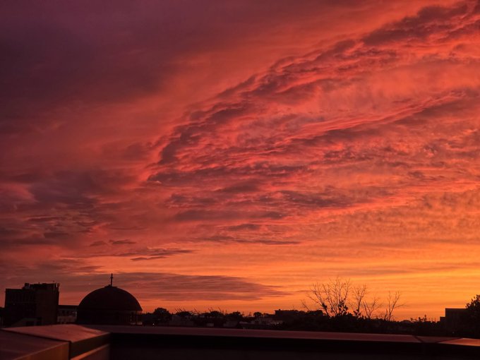 A dramatic sunset sky with vivid red and orange clouds over a city skyline featuring a domed building silhouette.