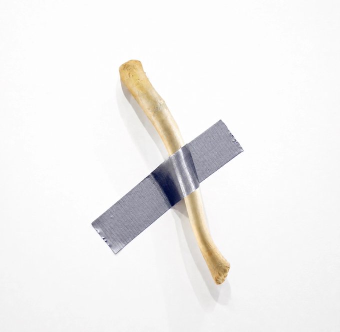 A pale, bone-like cylindrical object is crossed perpendicularly by a strip of gray duct tape against a plain white background.