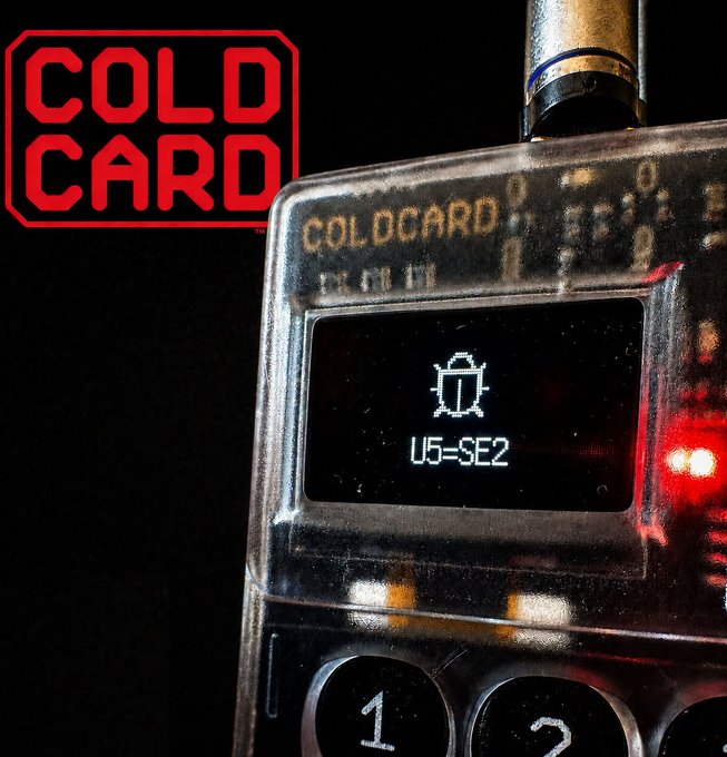 Close-up product photo of a transparent COLDCARD Mk4 hardware wallet device displaying 'US-SE2' on its small screen, with a red 'COLD CARD' stamp logo overlaid on the image.