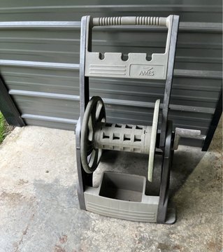 An Ames brand vintage-style hose reel mounted on a wall, featuring a hand crank, wheels, and a storage compartment.