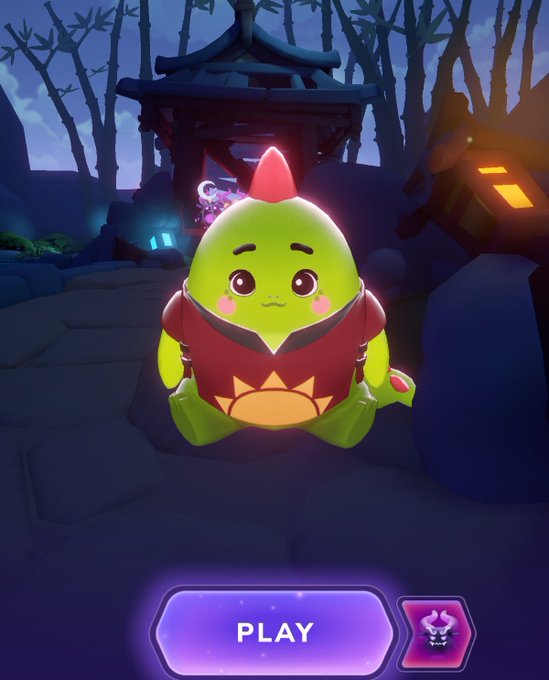 The image features a small green dinosaur character sitting on some rocks, possibly at the bottom of a cliff or mountain. The dinosaur has a red headband with a pink flower on top, giving it a unique appearance. In front of the dinosaur is a purple button that says "PLAY" in white letters.