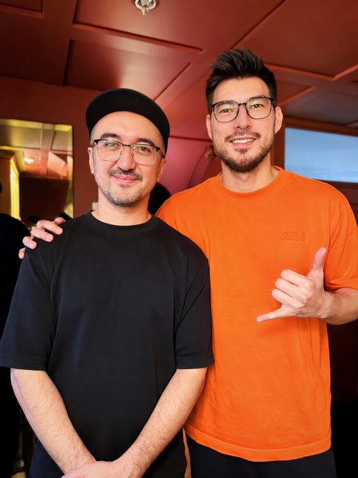 Two men pose together smiling, one wearing a black cap and shirt, the other in an orange Nike t-shirt making a hand gesture, likely at a Bored Ape Yacht Club (BAYC) event, with the post expressing excitement about the meetup and upcoming alphas.