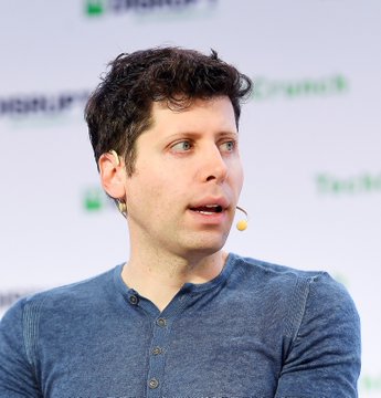The image shows a man with curly dark hair wearing a blue henley shirt and a headset microphone, appearing to speak at what looks like a TechCrunch event. The caption relates to the post by humorously framing the speaker as the face of "building a new kind of coworker," playing on the joke about AI chatbots becoming workplace collaborators rather than just smart conversational tools.