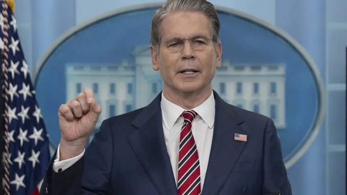 Treasury Secretary Scott Bessent speaks at a White House press briefing podium, gesturing as he addresses reporters. The image relates to the announcement of expanded U.S. debt buybacks potentially exceeding $4 billion, a key step in addressing the $35 trillion national debt.