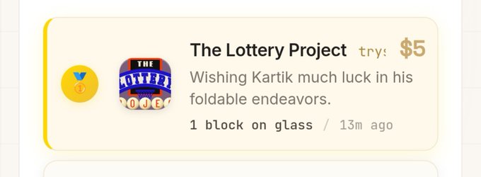 A screenshot of 'The Lottery Project' showing a $5 try entry wishing Kartik much luck in his foldable endeavors, with a 'O.J.E' icon.