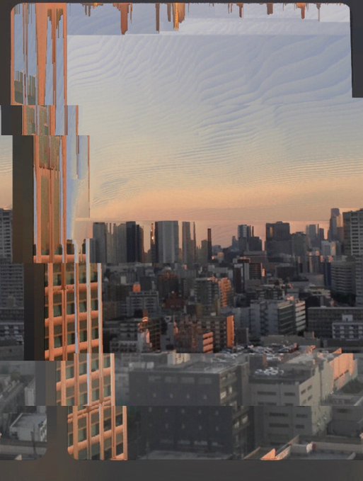 A glitched, digitally distorted image of a cityscape at sunset or sunrise shows tall buildings and a rippled sky, with rectangular blocks of misaligned pixel data on the left side.
