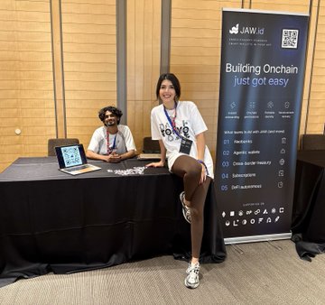 Two people are at the JAW stand during day one of ETHGlobal Tokyo, featuring a promotional banner that reads "Building Onchain just got easy," with the woman giving a thumbs-up while showing off the passkey wallet demo setup on the table.