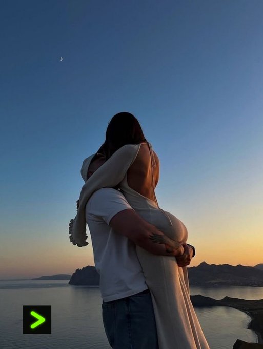 A romantic photo of a couple embracing at sunset by the sea, with the crescent moon visible in the sky above them.