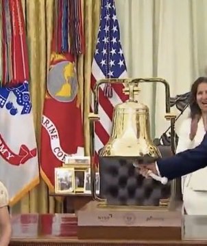 A woman in a white jacket reaches out to ring a large brass bell displayed on a wooden stand, surrounded by American flags and military service banners in the background. The post's reference to the "bell" appears to be a humorous or skeptical comment, as the bell is clearly visible in the image being rung.