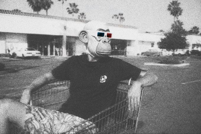 The image features a man wearing a gorilla mask, sitting inside a shopping cart with his arms crossed. The man appears to be bored or disinterested as he looks out of the cart window. The caption "GM bored ape yacht club" suggests that this scene might have been captured at a GM bored apes yacht club event or gathering where people dressed in gorilla masks are participating in various activities, such as shopping or socializing.