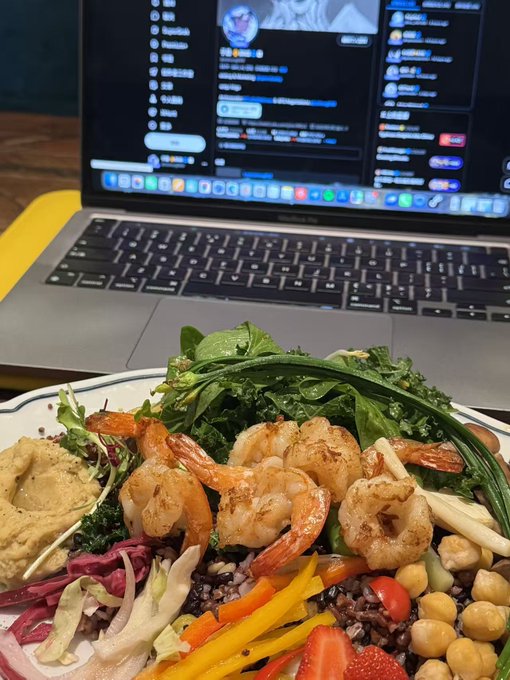 A shrimp and kale Buddha bowl sits in front of an open MacBook, illustrating a disappointing $10 lunch that the poster deemed not worth the price compared to cheaper Shaxian alternatives, while sharing a relieved update on $CETS reaching an all-time high.