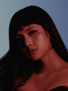 A moody close-up portrait of a young woman with long dark hair and bangs, softly lit against a dim background.