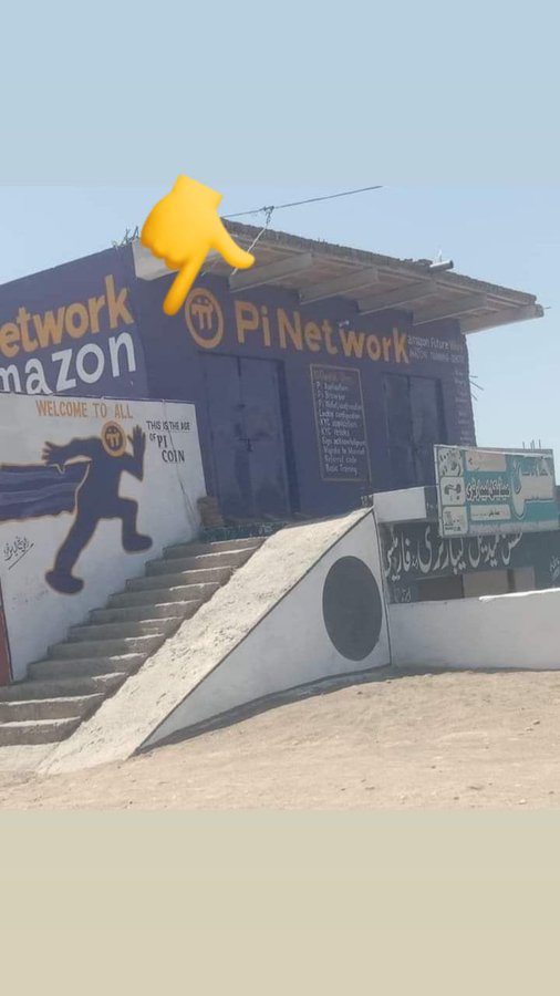 A building features hand-painted signs for "Pi Network" and "Amazon," with a Pi coin mascot graphic and the slogan "Welcome to all, this is the rise of Pi coin," hinting at rumors of an upcoming Amazon partnership with the cryptocurrency project.