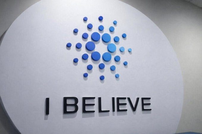 A white circular sign displays a cluster of blue dots arranged in a diamond pattern above the text 'I BELIEVE'.
