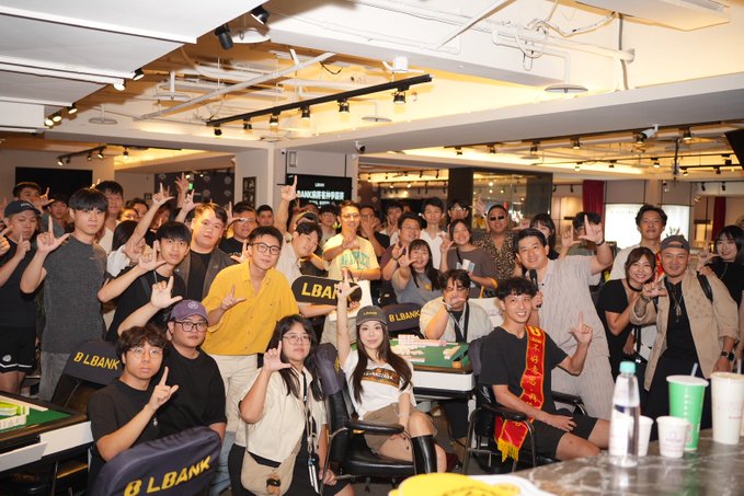 A large group of people pose together making rock-on signs at what appears to be an LBank office event, with visible "LBANK" branding on equipment, chairs, and signage throughout the room, celebrating the post about the author graduating from their role at @LBankchinese after handling marketing for the Chinese-speaking overseas region.
