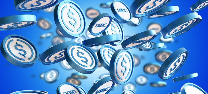 A 3D graphic illustration of numerous silver USDC stablecoin tokens floating and falling against a bright blue background.