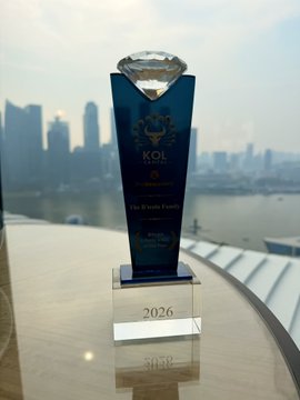 A blue glass trophy engraved with "KOL," "Bitcoin Lifestyle KOL of the Year," and the year "2026" sits on a reflective surface with a city skyline and river visible in the background, representing the personal Bitcoin journey and lifestyle award mentioned in the post.