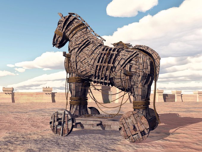 A wooden Trojan horse sculpture on wheels stands in a desert landscape beneath a partly cloudy sky.