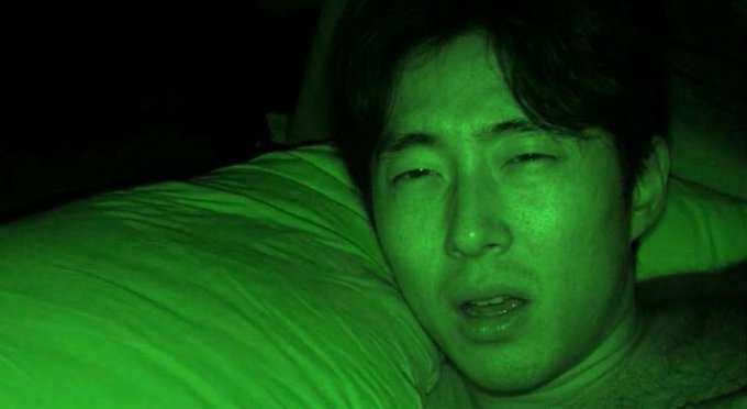 A close-up shot of a person's face illuminated by a strong green light in a dark setting, with their eyes partially closed and mouth slightly open.