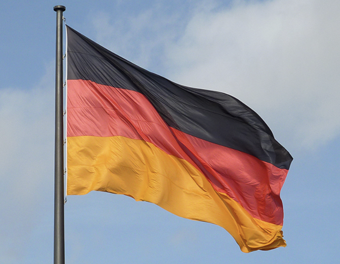 The German flag waves against a blue, cloudy sky, symbolizing Germany as the country at the center of a reported policy shift to end its one-year crypto tax exemption in the 2027 budget.