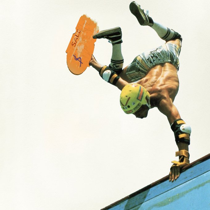 A skateboarder performs an aerial trick on a ramp, holding an orange board marked "SALE" while wearing a yellow helmet, knee pads, and elbow pads.