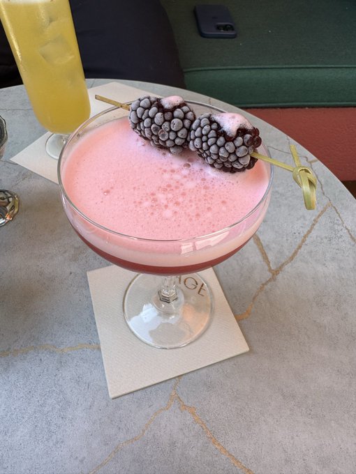 iced tea with a slice of lemon and two blackberries on the rim, accompanied by a glass of pink cocktail with a straw and garnish.