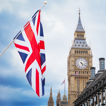 A Union Jack British flag waving in the foreground with the iconic Big Ben clock tower visible against a cloudy sky in London.