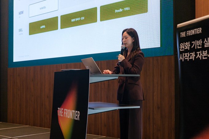 A woman in a dark blazer speaks into a microphone at 'THE FRONTIER' podium, with a slide behind her showing company categories including 'KRAFTON', 'PEARL ABYSS', and Korean market sections.