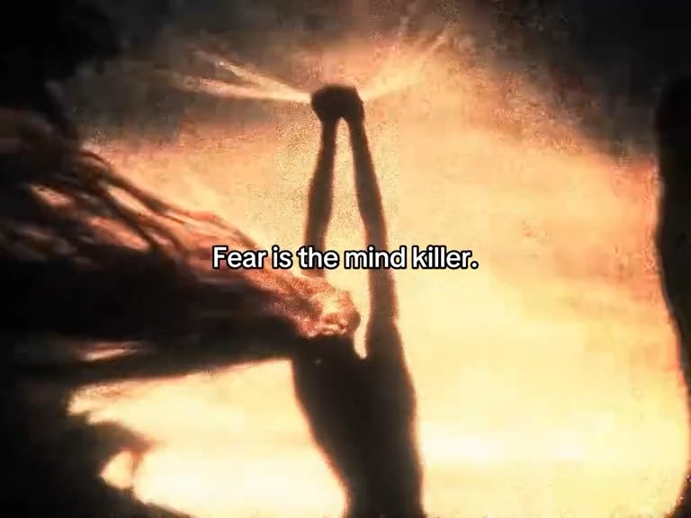 A cinematic still showing a silhouetted figure with raised arms against a dramatic orange/golden background with the text "Fear is the mind killer."