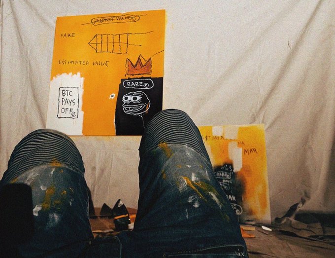 An artist's legs in paint-stained jeans rest in front of canvases, with the prominent orange painting displaying handwritten text including "FAKE," "ESTIMATED VALUE," "BTC PAYS OFF," and "RARE."