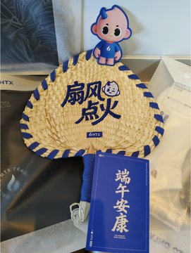 The image features a fan with blue and white colors, as well as a book that has Chinese characters on it. The fan appears to be made of straw or bamboo material, while the book seems to have an Asian theme. Both items are placed next to each other in the scene.