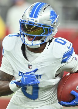 A Detroit Lions football player wearing a white jersey with the number 9 and a silver helmet with blue stripes, running with a football.