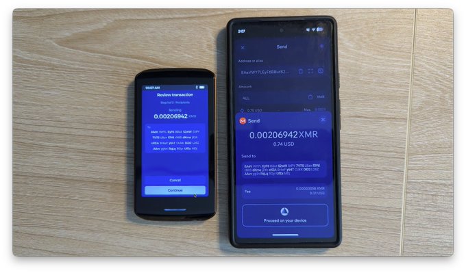 Two smartphones rest on a wooden surface displaying a Monero (XMR) transaction of 0.00206942 XMR (~$0.24 USD), with the smaller device on the left showing a "Review transaction" screen ready to confirm, while the larger phone on the right displays the "Send" interface prompting to "Proceed on your device" — illustrating the Bluetooth-based signing flow between the Passport Prime hardware wallet and Cake Wallet app mentioned in the post.