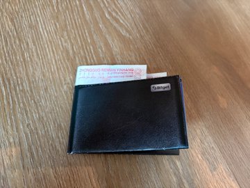 The image shows an open wallet with a crisp 100-yuan bill inside. The bill appears to be crumpled, indicating that it has been used or handled recently. The wallet is placed on a wooden surface, possibly a table or countertop. The text in the image reads "Dude, am I seeing this right??! How did a crisp hundred-yuan bill in my hand turn into worthless scrap paper? Wangzai and Bitget are teaming up to remind everyone: In a bear market, the most important thing has never been how much you make—it'S about not losing your principal."