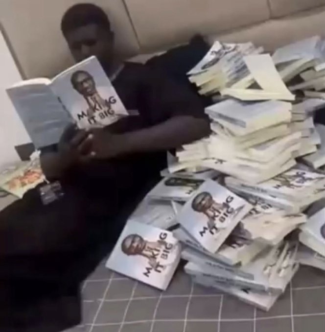 A man sits on a couch reading a book titled 'MAKING IT BIG' surrounded by massive stacks of paper money and additional copies of the same book.