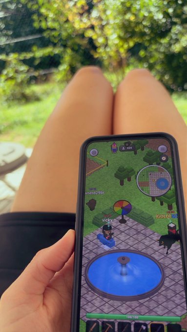 A first-person view of someone playing the mobile game 'Habbo' on their phone while sitting outdoors, with their bare legs visible in the background.