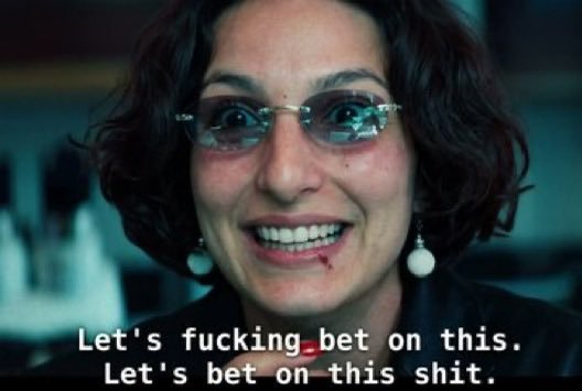 A cinematic close-up of a woman with short dark hair and glasses, smiling with a small amount of blood on her lip, with subtitles reading 'Let's fucking bet on this. Let's bet on this shit.'