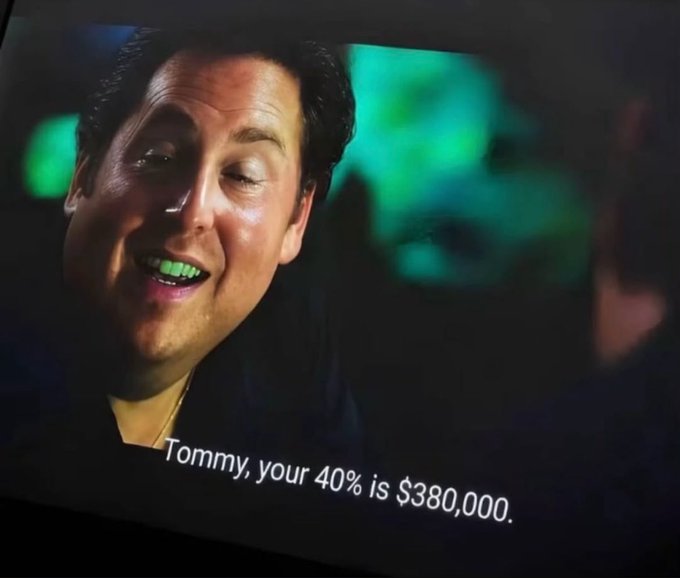 A man smiles with his eyes closed while green smoke is visible in the background, with subtitles reading 'Tommy, your 40% is $380,000.'