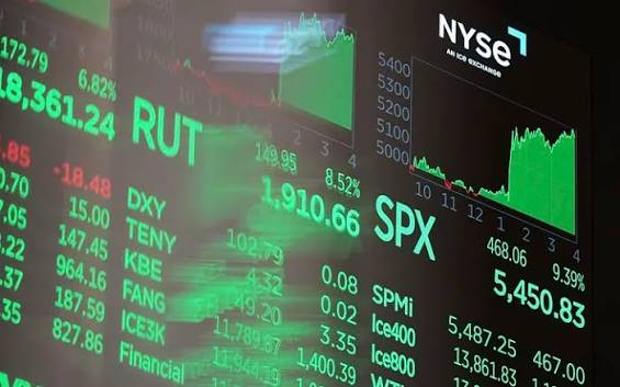 A close-up of the NYSE stock ticker board displaying various financial indices and stocks in bright green text, including RUT, SPX at 5,450.83, DXY, SPmi, and ICE800, with a line chart in the upper right.