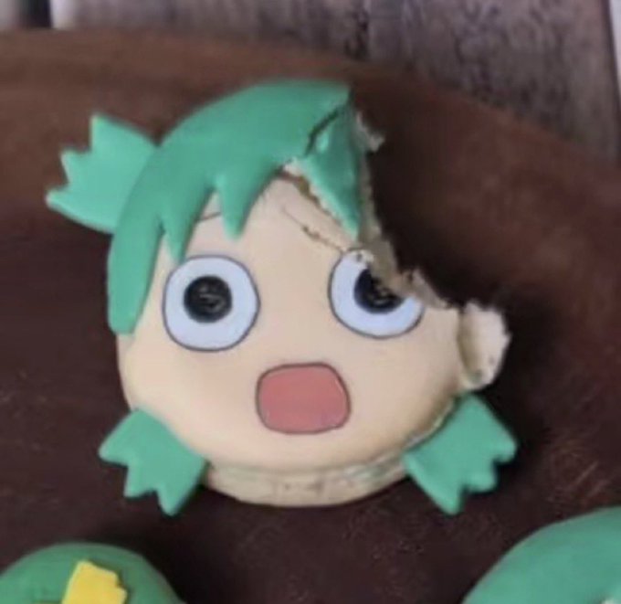 A damaged Yotsuba-chan plush figure with green hair, showing torn fabric and stuffing coming out, with a shocked facial expression.