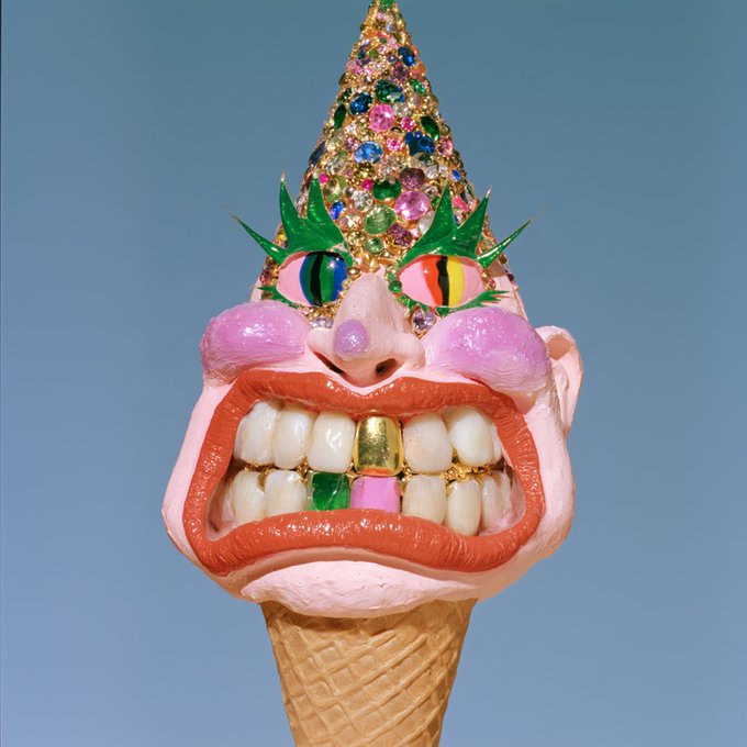A surreal, colorful art piece depicting a face made from an ice cream cone, featuring a jeweled cone hat, multicolored eyes, pink cheeks, and a mouth with a single gold tooth.