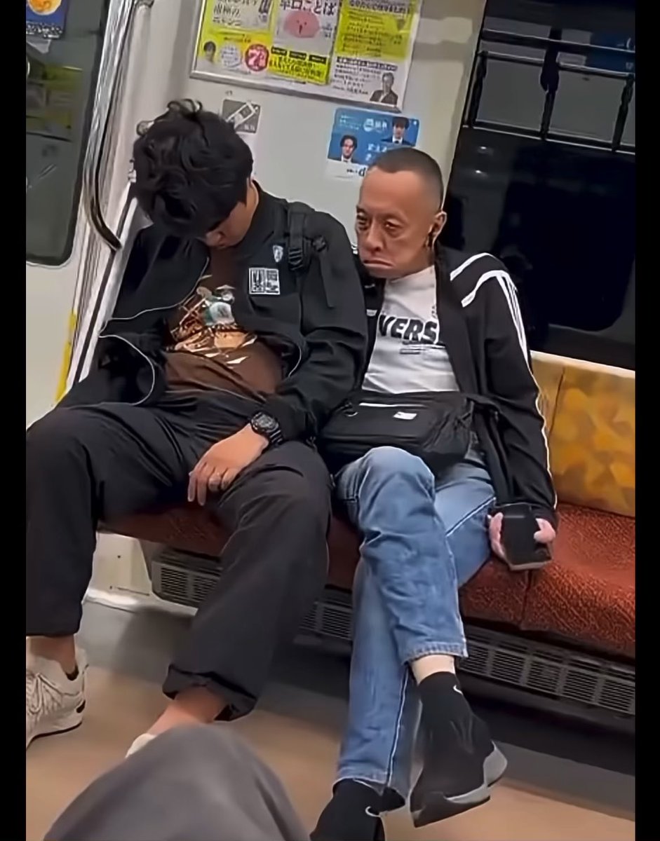 On a Japanese train, two exhausted commuters sit slumped together — one sleeping with his head bowed in a black jacket, the other staring blankly ahead in a striped shirt reading "VERS" — visually mirroring the post's message about crypto victims being "asleep" and oblivious while shady operators quietly pick their pockets like pickpockets on public transit.