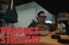 A man with glasses sits in an office setting with a camera in the foreground, overlaid with bold red text reading 'PRODUCT STRATEGY'.