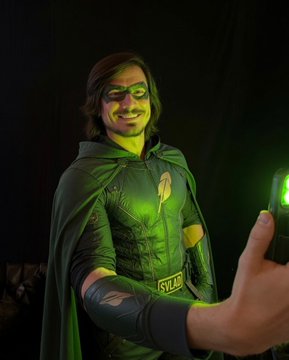 A smiling man dressed in a green superhero costume with a cape poses dramatically as his outstretched hand glows bright green, mirroring the meme's $VLAD ticker reference to Vlad Tenev, CEO of Robinhood, while playfully tying the Robinhood Chain memecoin branding to a heroic "Green Lantern"-style aesthetic.