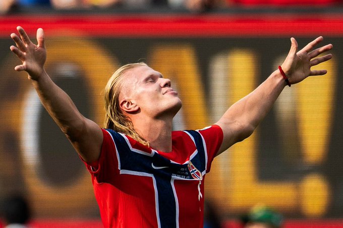 A soccer player in a red Norway jersey celebrates with arms outstretched and head tilted back, with "GOAL!" visible in the background—capturing the "YYDS" (eternal god/GOAT) moment of triumph as he soaks in the glory of a crucial score.
